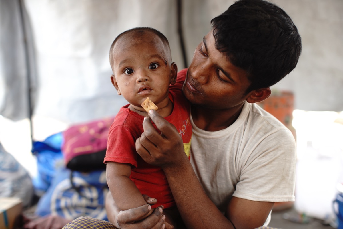 Rohingya refugee father feeding his son a WFP high-energy biscuit